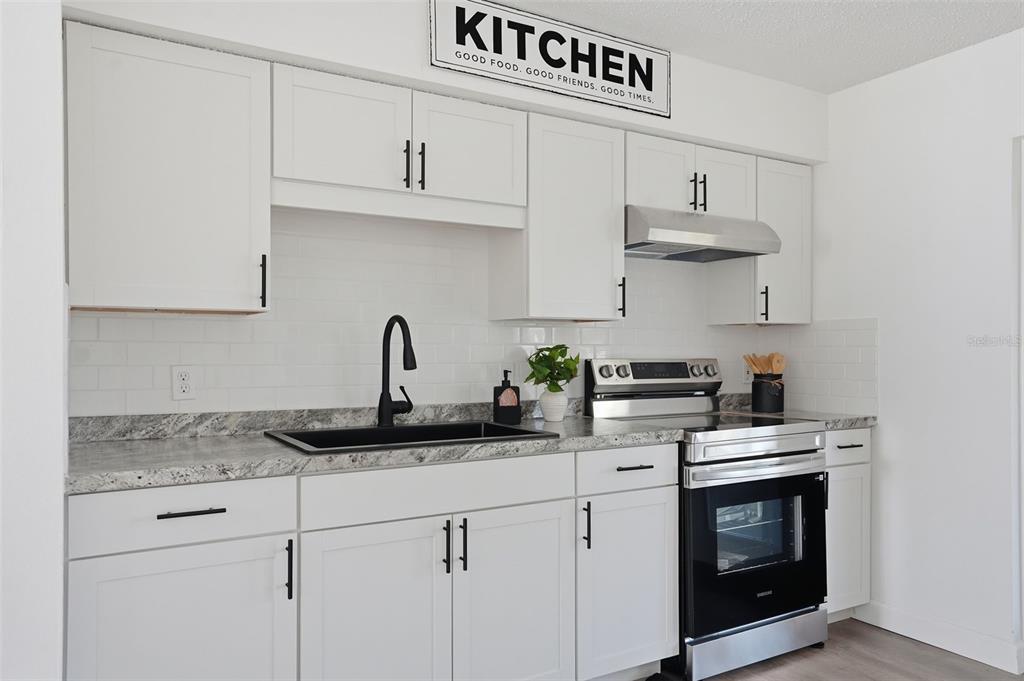 A kitchen features white cabinets, granite countertops, a black sink, and stainless steel appliances — 2076 LANDOVER BOULEVARD, SPRING HILL, FL