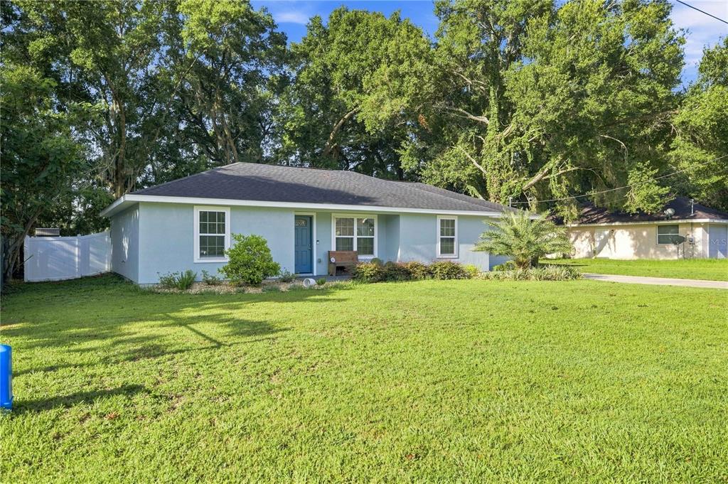 A light blue single-story house with a dark roof sits on a large grassy lawn — 1864 NE 126TH LANE, ANTHONY, FL