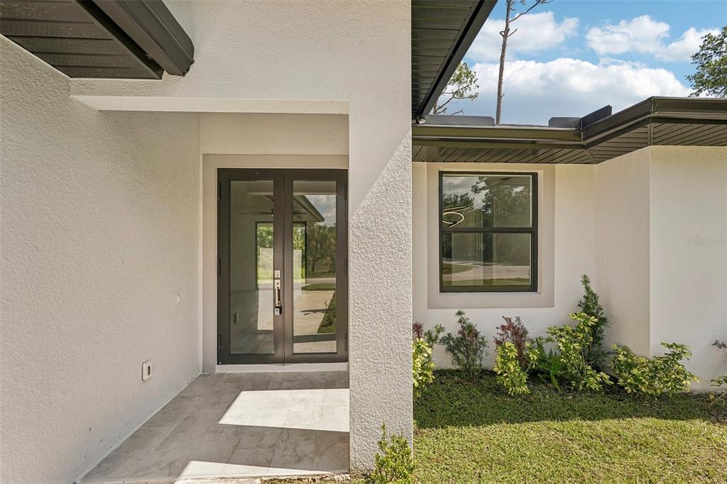 A modern home entrance features a white stucco exterior, double glass doors, and a window — 17156 EUGENE AVENUE, PORT CHARLOTTE, FL