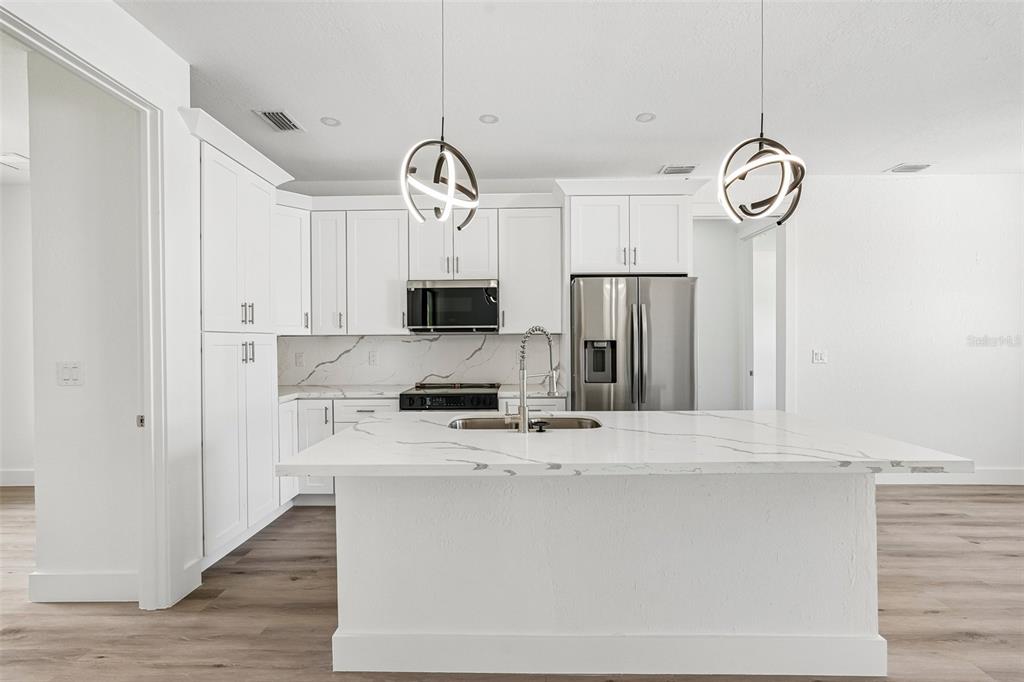 A modern white kitchen features a large marble-topped island, stainless steel appliances, and pendant lighting — 17156 EUGENE AVENUE, PORT CHARLOTTE, FL