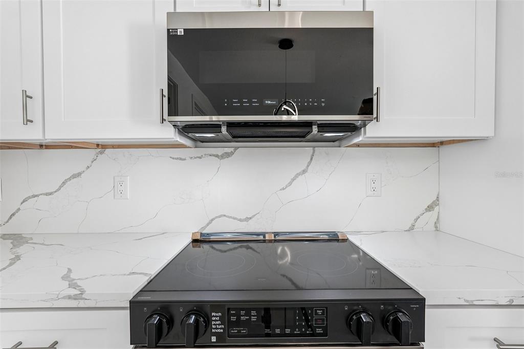 A kitchen features white cabinets, a marble-patterned backsplash, and a black microwave over a range — 17156 EUGENE AVENUE, PORT CHARLOTTE, FL