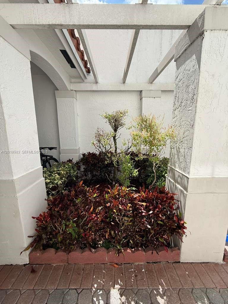A small garden bed with shrubs and trees sits beneath a white pergola structure — 10973 NW 62nd Ter, Doral FL 33178, DORAL, FL