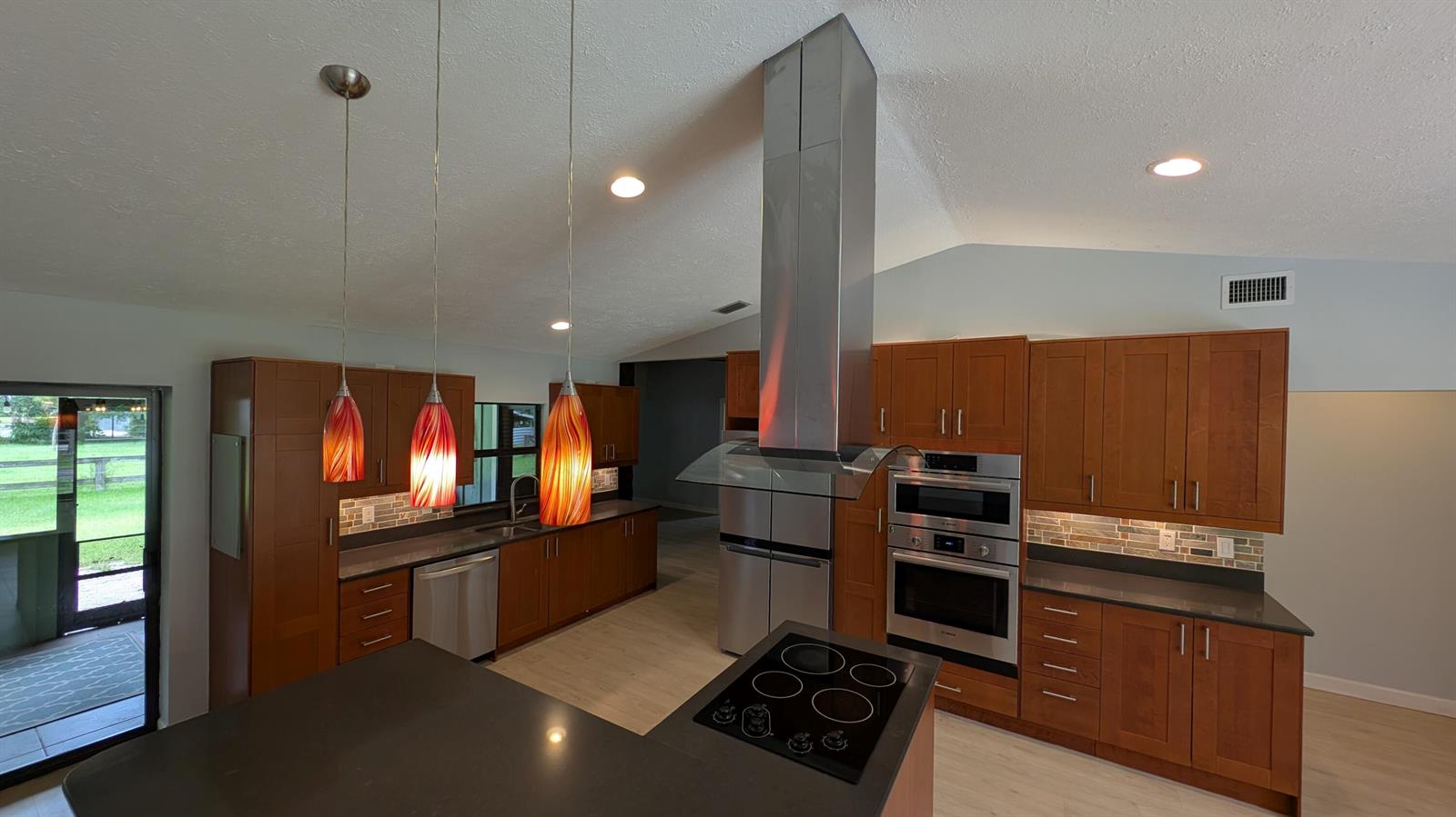 A kitchen features wood cabinets, stainless steel appliances, a center island, and three pendant lights — 10173 150th Court N, Jupiter FL 33478, JUPITER, FL