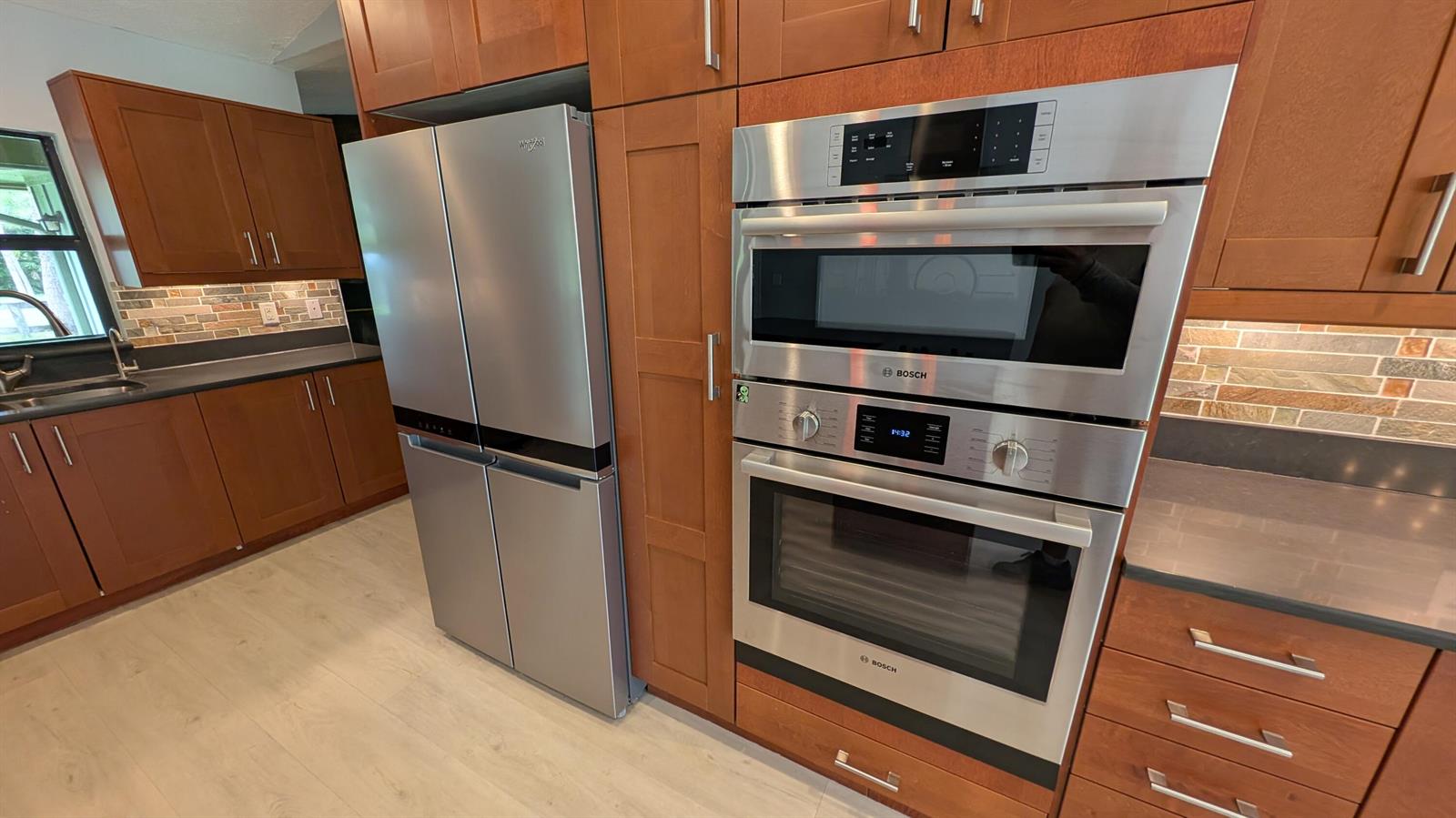 A kitchen features stainless steel appliances, wood cabinetry, and a stone tile backsplash — 10173 150th Court N, Jupiter FL 33478, JUPITER, FL