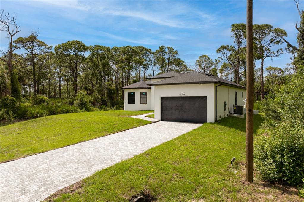 A modern single-story house with a paved driveway and a dark garage door — 12086 CHAMBERLAIN BOULEVARD, PORT CHARLOTTE, FL