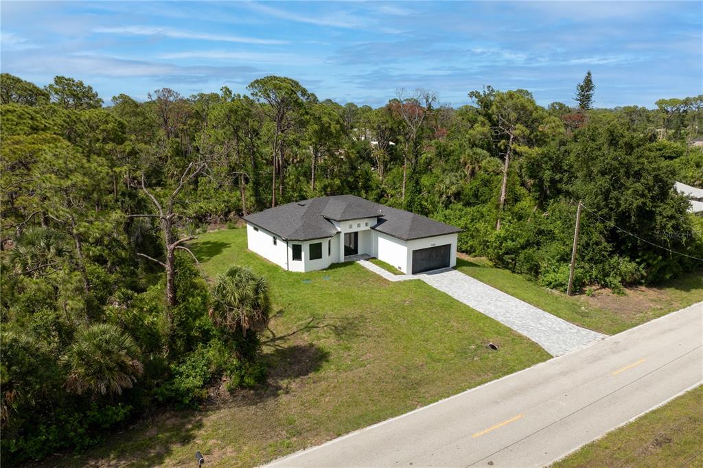 An aerial view shows a modern white house with a dark roof and paved driveway — 12086 CHAMBERLAIN BOULEVARD, PORT CHARLOTTE, FL