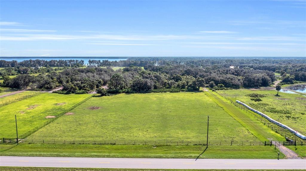An aerial view shows a large, fenced grassy lot bordered by trees and a road — CANOE CREEK ROAD, ST CLOUD, FL
