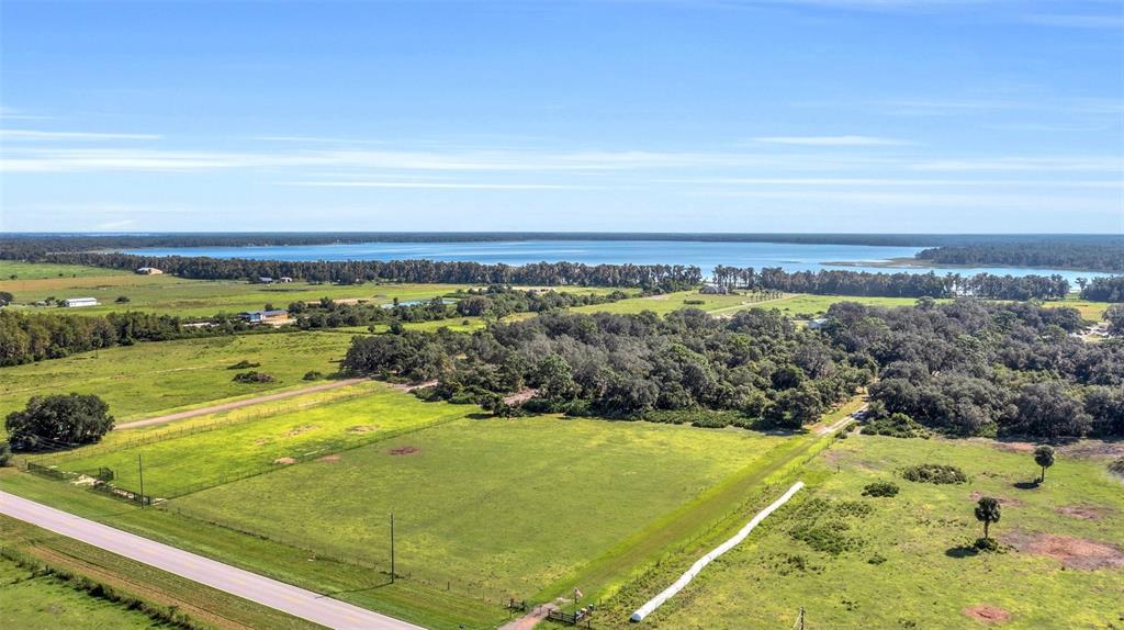 An aerial view shows a large grassy field with trees and a lake in the distance — CANOE CREEK ROAD, ST CLOUD, FL