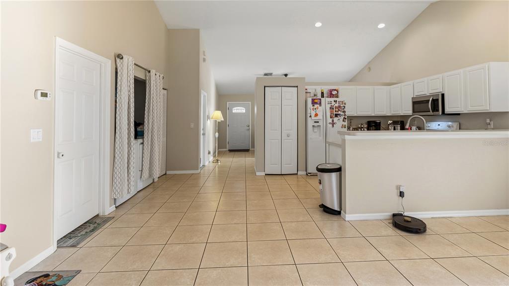 A kitchen with white cabinets and a tile floor opens into a living area — 2001 SW FEARS AVENUE, PORT ST LUCIE, FL