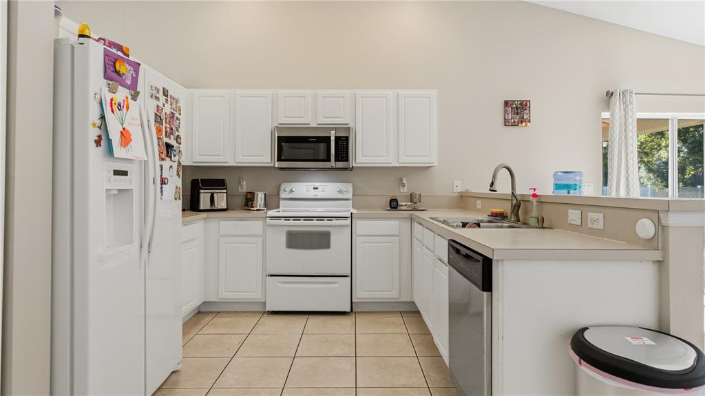 A kitchen with white cabinets, white appliances, tile flooring, and a peninsula sink — 2001 SW FEARS AVENUE, PORT ST LUCIE, FL