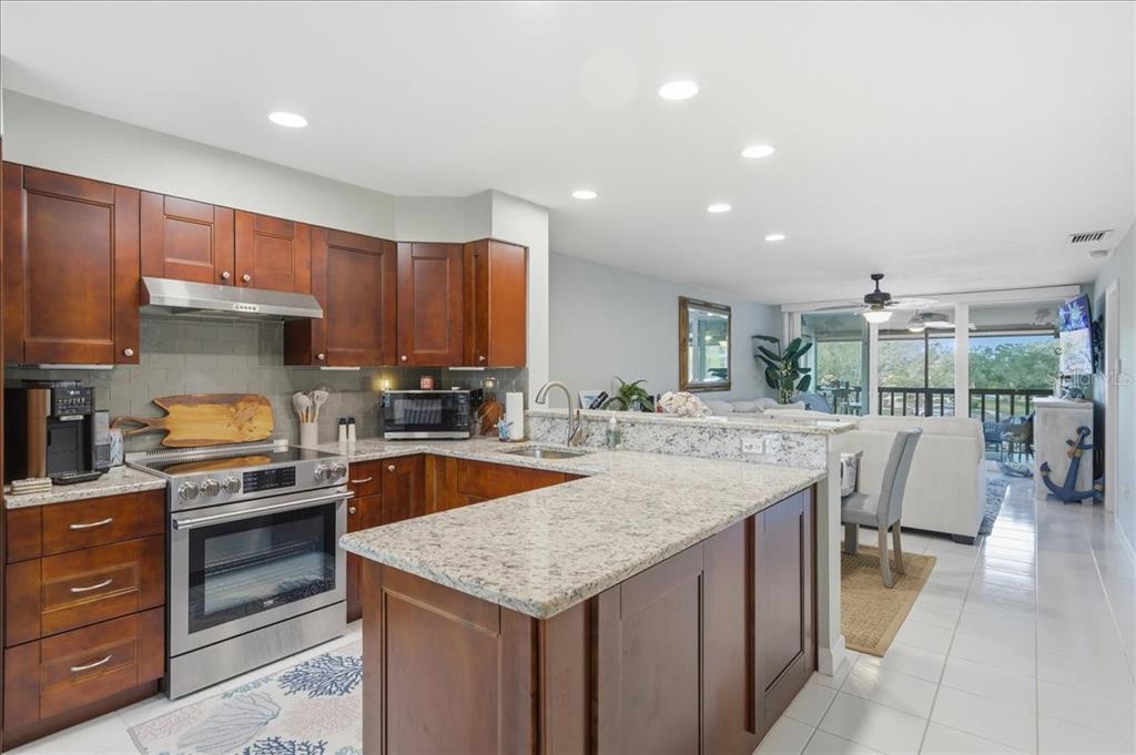 A kitchen with cherry wood cabinets, granite countertops, and stainless steel appliances overlooks a living area — 1802 MARINER DRIVE UNIT 30, TARPON SPRINGS, FL