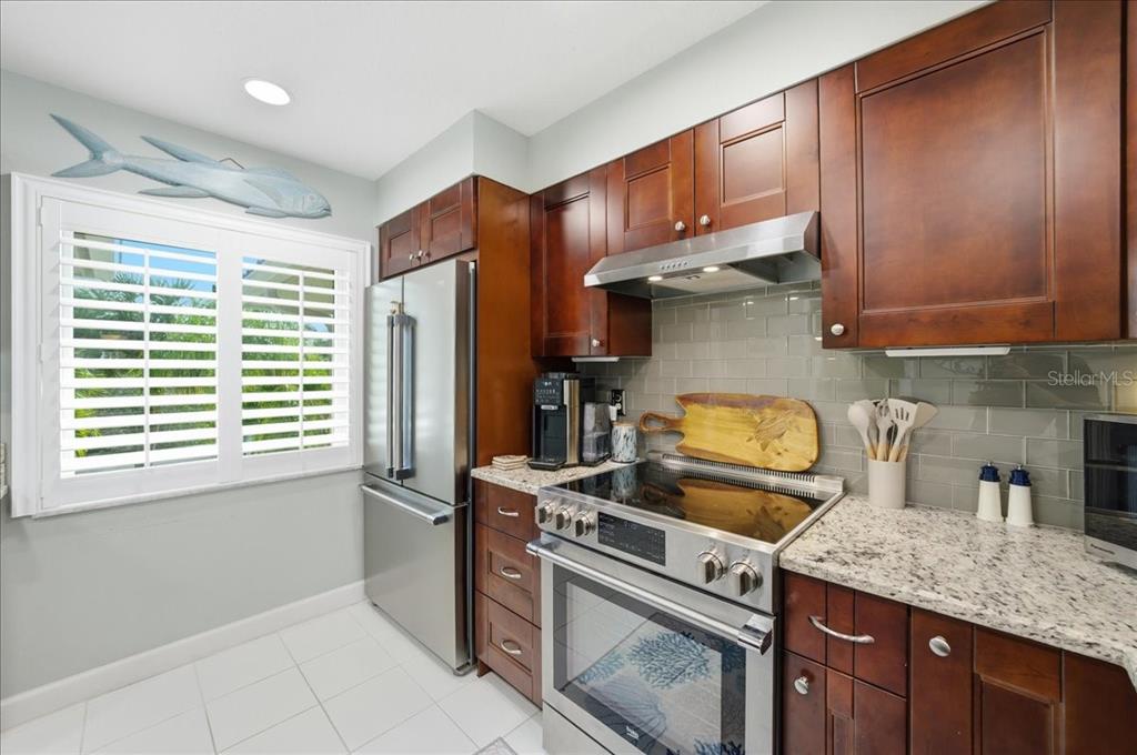 A kitchen with dark wood cabinets, stainless steel appliances, granite countertops, and gray tile backsplash — 1802 MARINER DRIVE UNIT 30, TARPON SPRINGS, FL