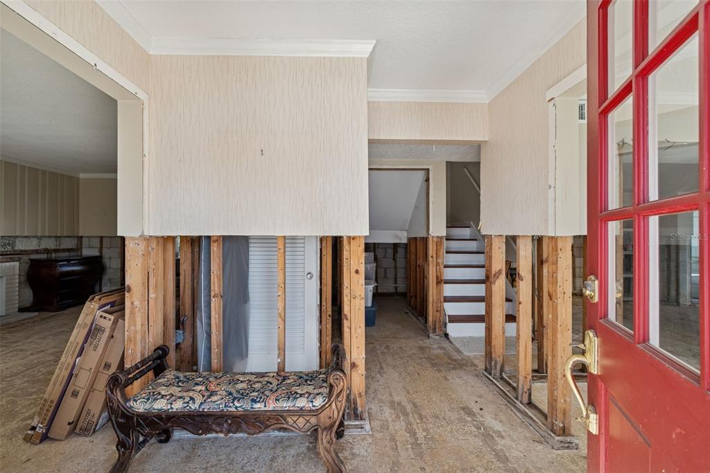 An entryway with exposed wall studs, a red door, and a staircase leading upstairs — 19 SANDPIPER ROAD, TAMPA, FL