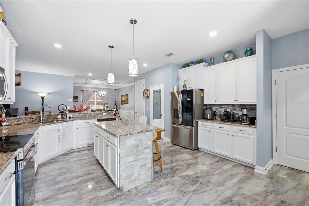 A kitchen with white cabinets, granite countertops, a center island, and light-colored tile flooring — 4020 CARTERET DRIVE, WINTER HAVEN, FL
