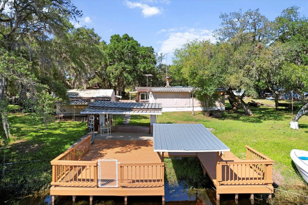An elevated wooden deck with a boat slip overlooks a grassy yard and a house — 8109 E TIERRA COURT, INVERNESS, FL