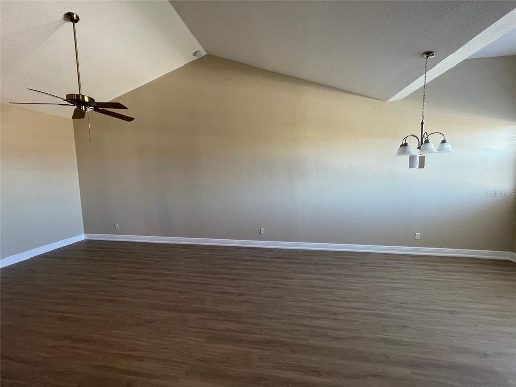 An empty room with vaulted ceilings, wood-look flooring, a ceiling fan, and a chandelier — 10365 PENDLETON AVENUE, ENGLEWOOD, FL