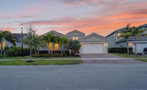A single-story suburban house with a two-car garage and palm trees at sunset — 15804 Goldfinch Circle, Westlake FL 33470, WESTLAKE, FL