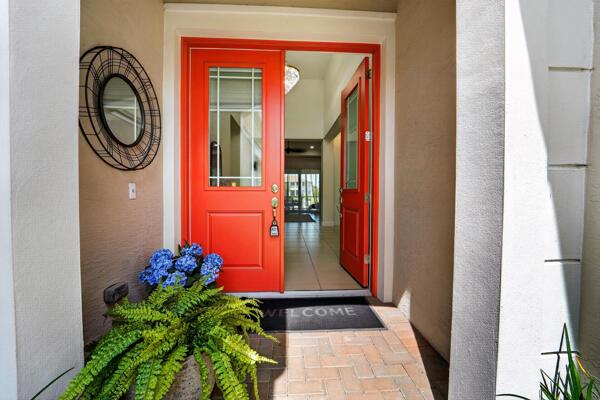 A bright orange front door opens into a tiled entryway with a decorative wall mirror — 15804 Goldfinch Circle, Westlake FL 33470, WESTLAKE, FL