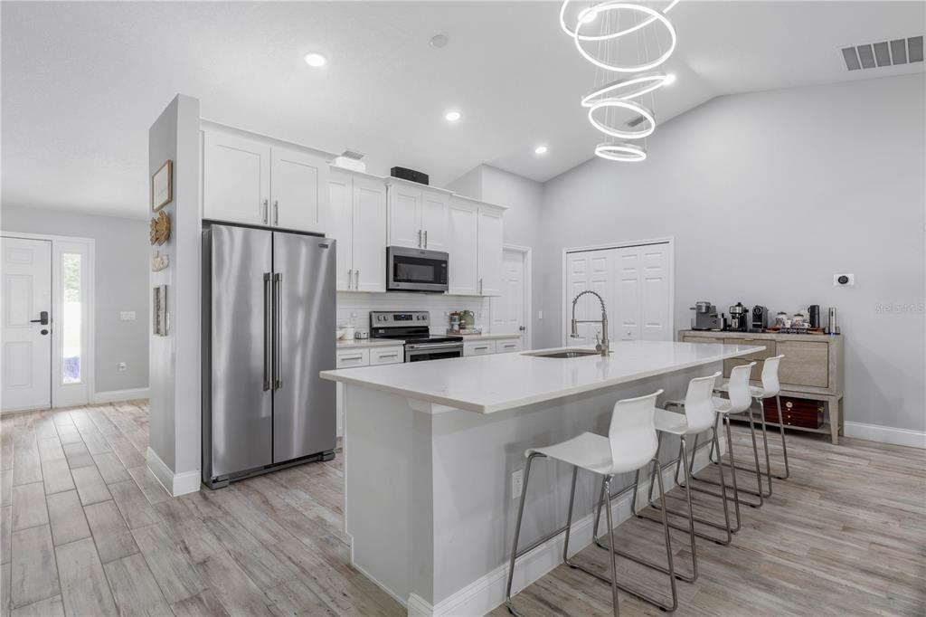 A modern kitchen features white cabinetry, stainless steel appliances, a large island, and wood-look flooring — 64 BOSTON LANE, PALM COAST, FL