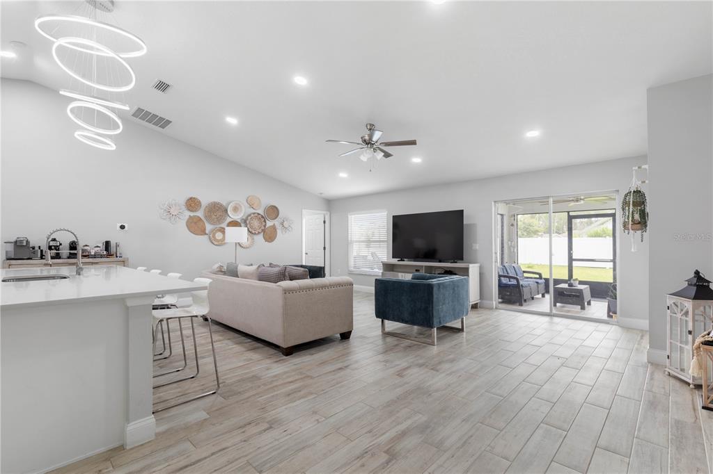 An open-concept living room features light wood-look tile flooring, a kitchen island, and sliding doors — 64 BOSTON LANE, PALM COAST, FL