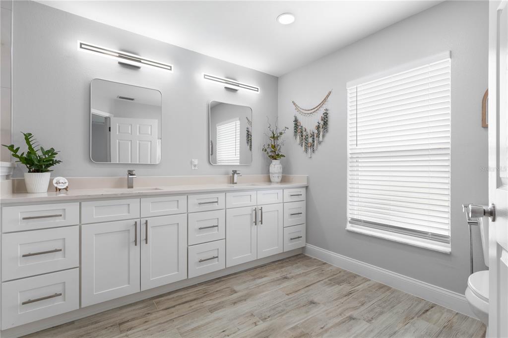 A bathroom features a double vanity with white cabinets, rectangular mirrors, and wood-look tile flooring — 64 BOSTON LANE, PALM COAST, FL