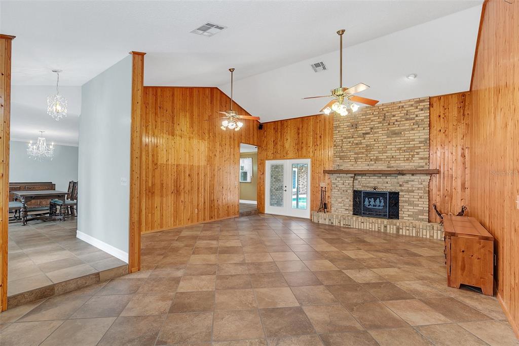 A living room features wood-paneled walls, a brick fireplace, and tile flooring under a vaulted ceiling — 4147 BOGGY CREEK ROAD, KISSIMMEE, FL