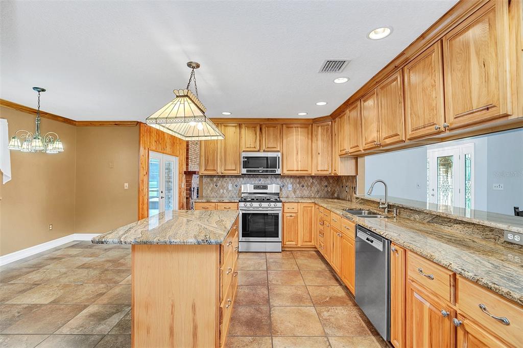 A kitchen with light wood cabinets, granite countertops, a center island, and tile flooring — 4147 BOGGY CREEK ROAD, KISSIMMEE, FL