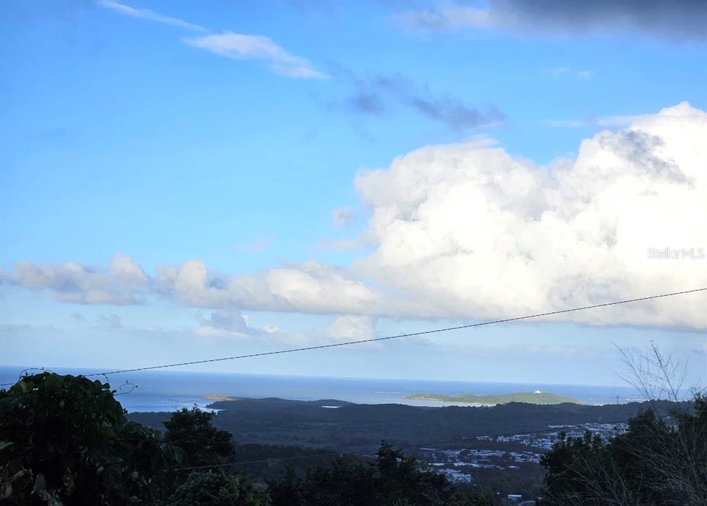 A high-angle view shows a coastal landscape with a distant island under a cloudy sky — 985 KM 1.6 INTERIOR QUEBRADA FAJARDO, FAJARDO, PR