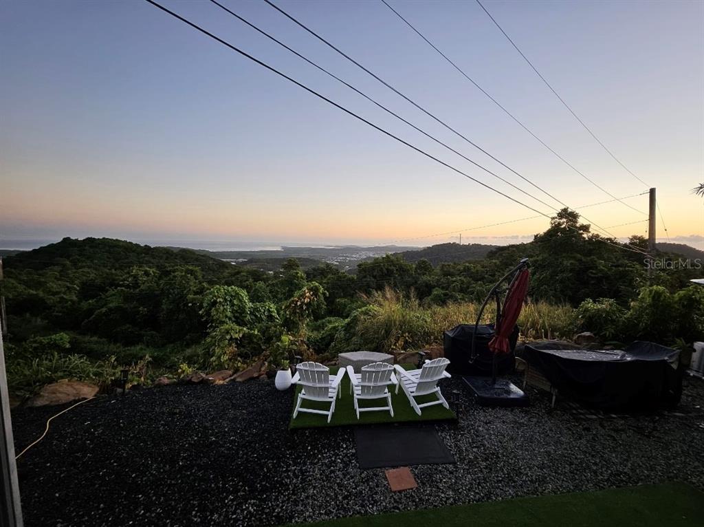 Three white chairs sit on a small patch of artificial turf overlooking a forested landscape — 985 KM 1.6 INTERIOR QUEBRADA FAJARDO, FAJARDO, PR