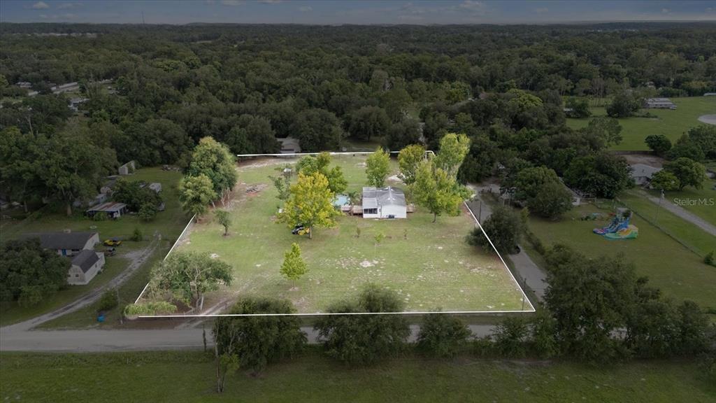An aerial view shows a single-story house situated on a large, grassy, tree-filled lot — 12936 MARSH ROAD, SPRING HILL, FL