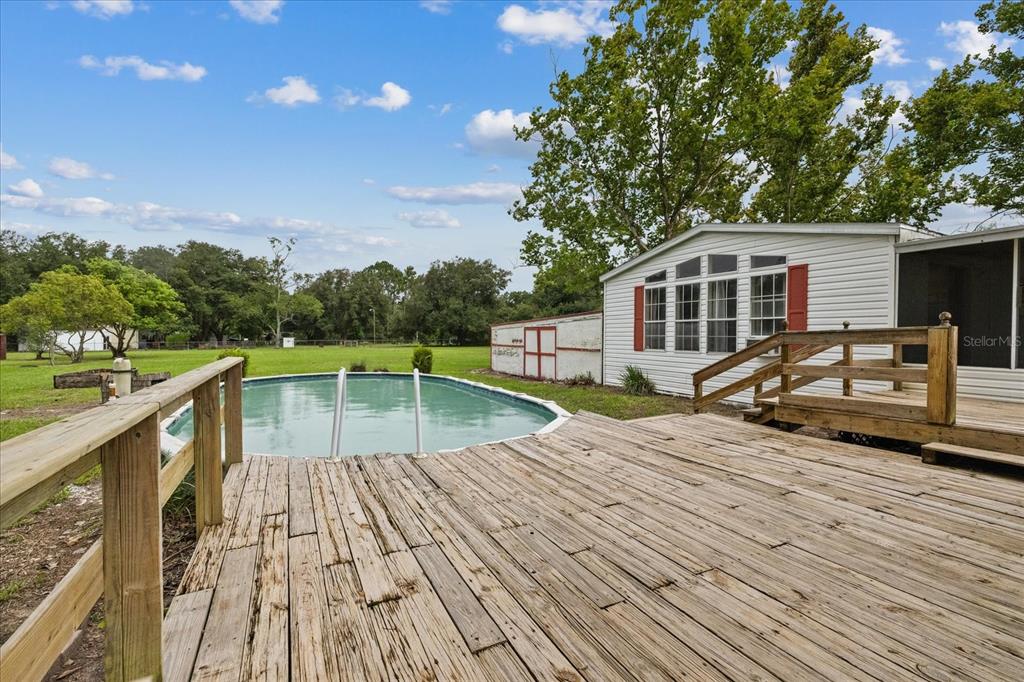 A wooden deck overlooks an above-ground swimming pool next to a white mobile home — 12936 MARSH ROAD, SPRING HILL, FL