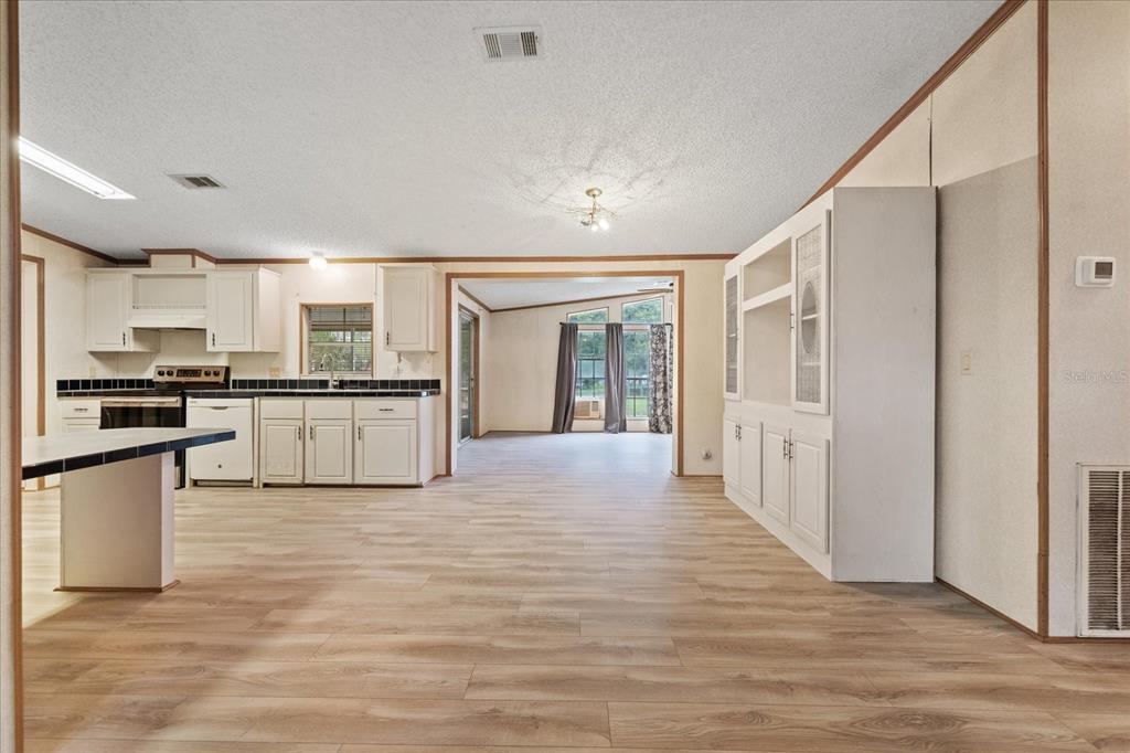 A kitchen and living area with white cabinets, light wood-look flooring, and a built-in hutch — 12936 MARSH ROAD, SPRING HILL, FL