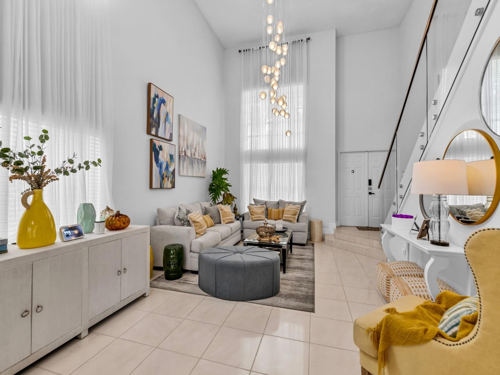 A bright, high-ceilinged living room features a modern chandelier, neutral furniture, and tiled flooring — 101 Gables Boulevard, Weston FL 33326, WESTON, FL