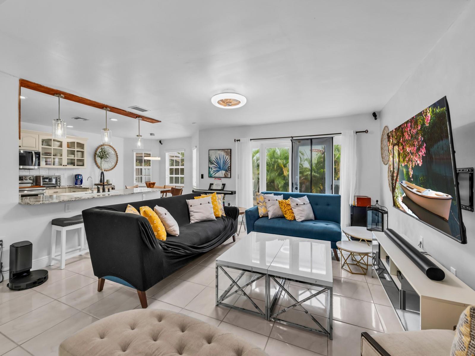 A living room with a black sofa, blue loveseat, white coffee tables, and an open kitchen — 101 Gables Boulevard, Weston FL 33326, WESTON, FL