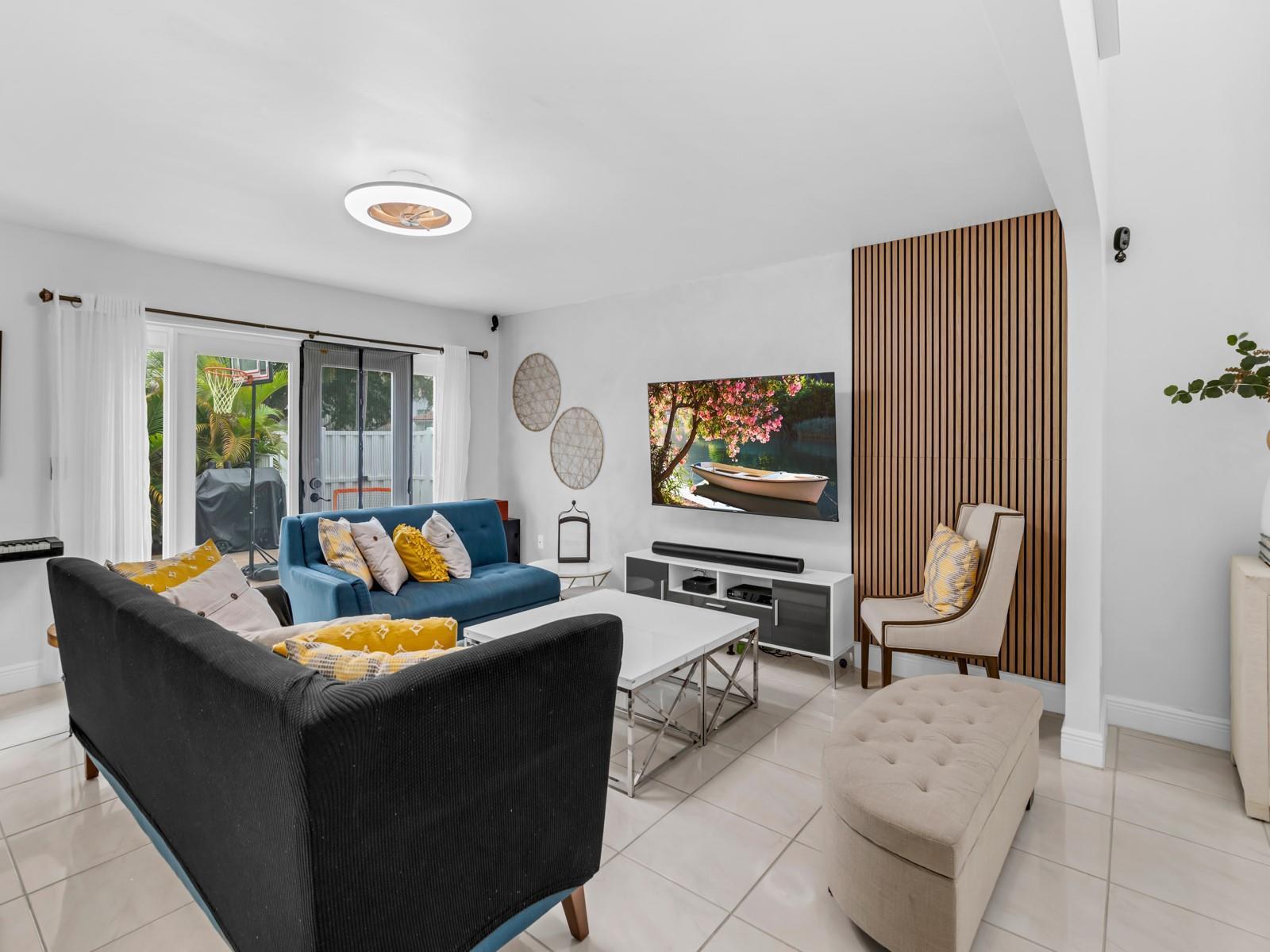 A living room features a blue sofa, a black sofa, and a wood-slatted accent wall — 101 Gables Boulevard, Weston FL 33326, WESTON, FL