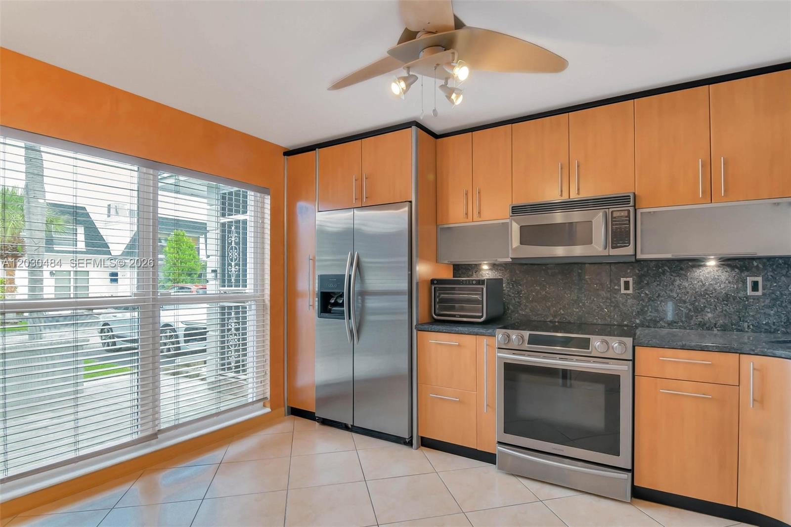 A kitchen features light wood cabinets, stainless steel appliances, dark countertops, and orange walls — 812 NE 26th Ave, Hallandale Beach FL 33009, HALLANDALE BEACH, FL