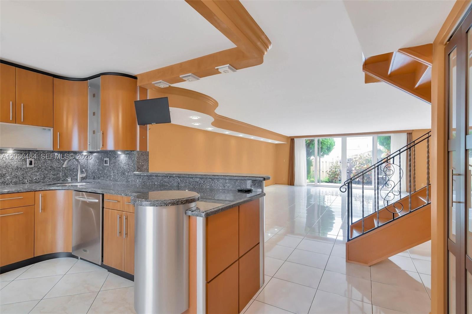 A kitchen with wood cabinets and granite countertops overlooks a living area with stairs — 812 NE 26th Ave, Hallandale Beach FL 33009, HALLANDALE BEACH, FL