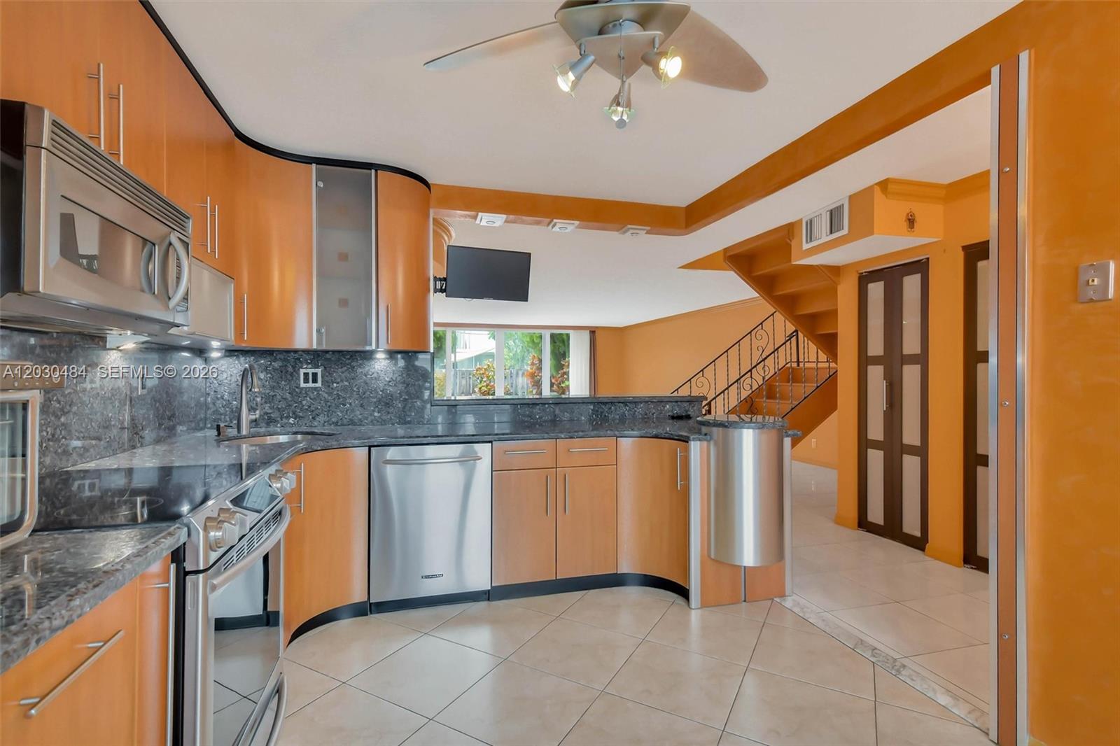 A kitchen with light wood cabinets, granite countertops, and stainless steel appliances overlooks a staircase — 812 NE 26th Ave, Hallandale Beach FL 33009, HALLANDALE BEACH, FL