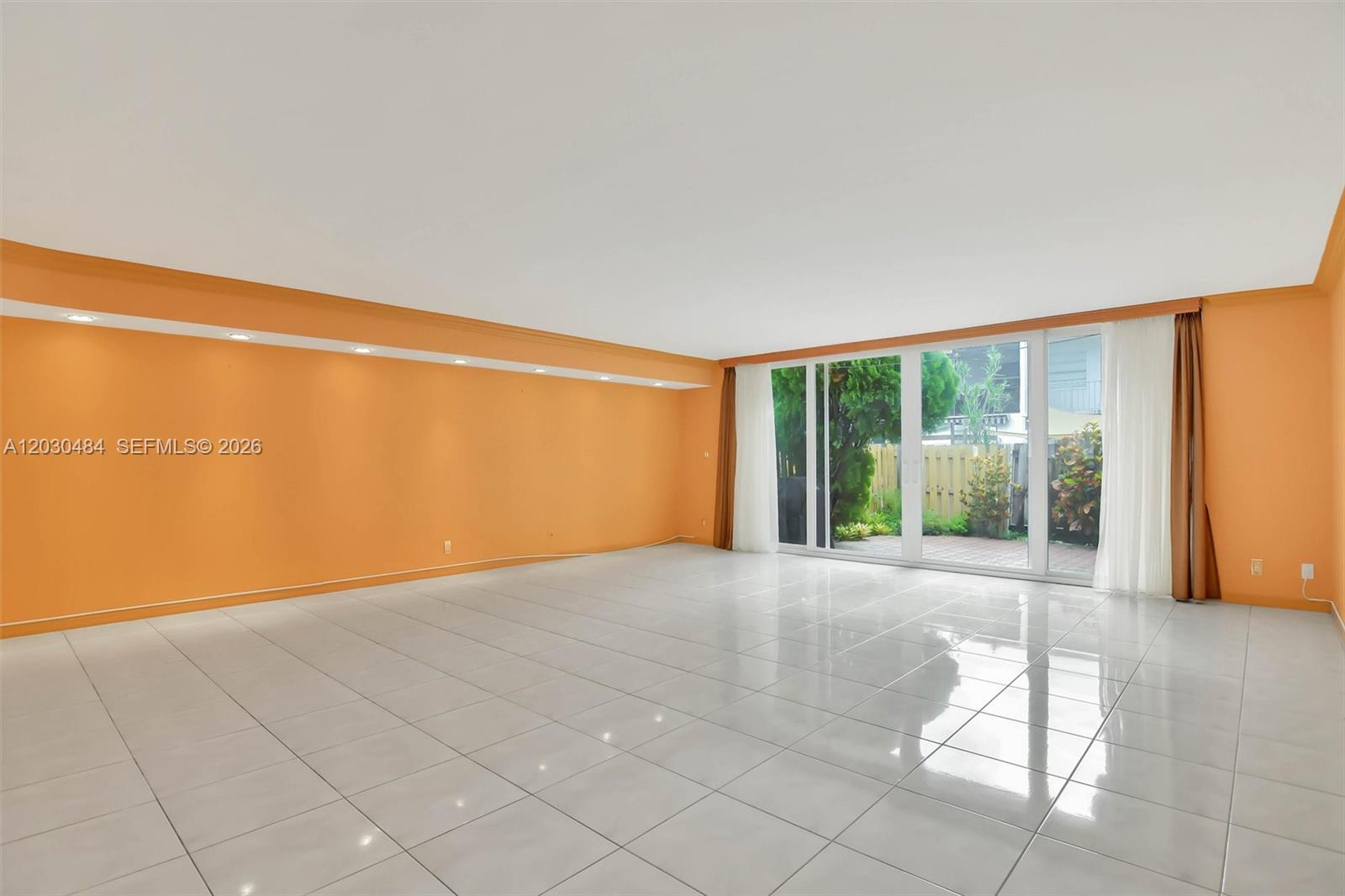 A spacious room features orange walls, white tile flooring, recessed lighting, and sliding glass doors — 812 NE 26th Ave, Hallandale Beach FL 33009, HALLANDALE BEACH, FL