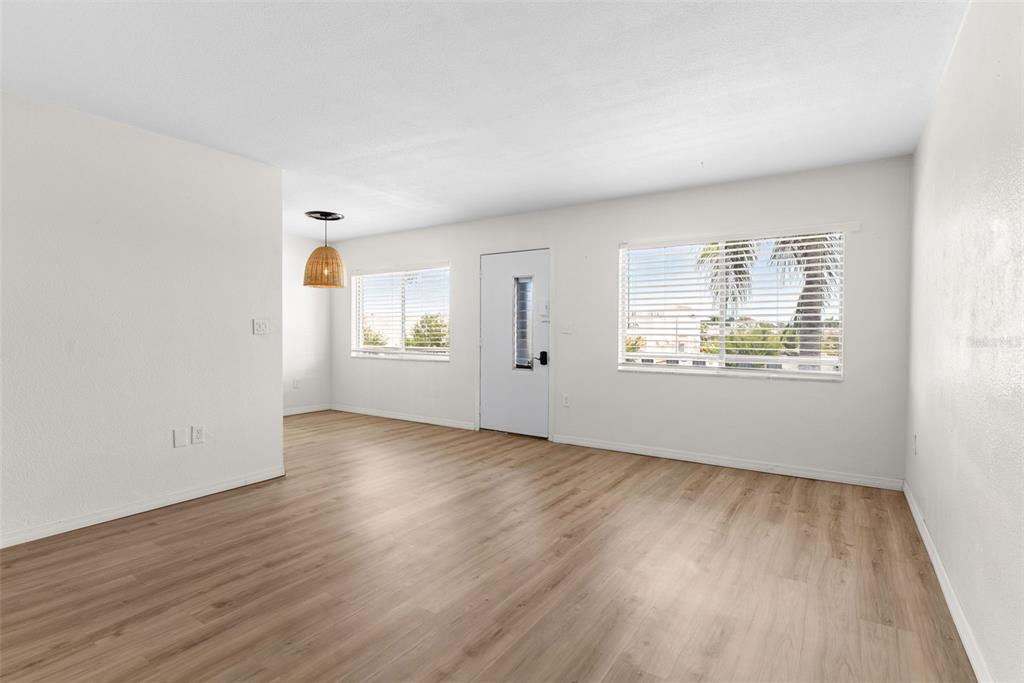 An empty living room features light wood-look flooring, white walls, and two windows with blinds — 11251 80TH AVENUE UNIT 307, SEMINOLE, FL