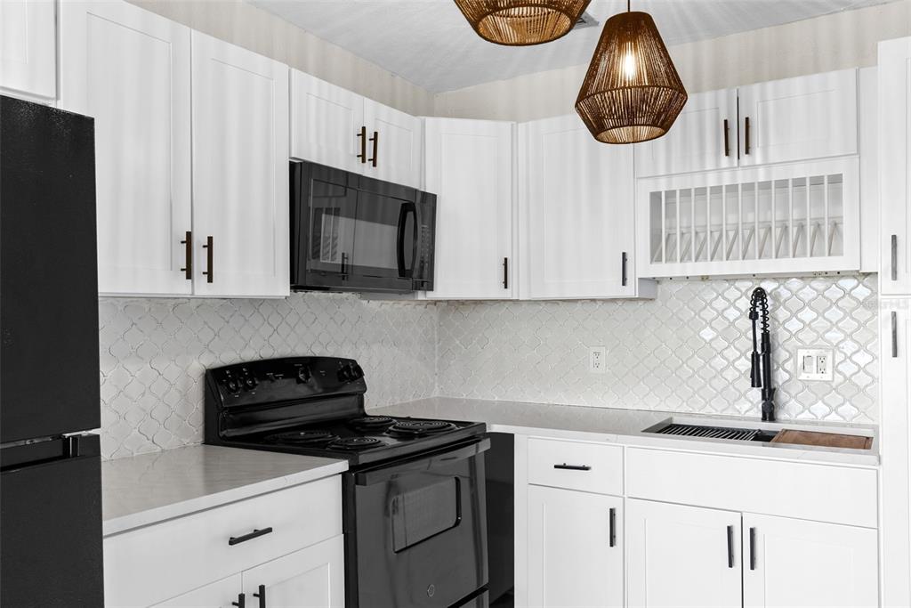 A kitchen features white cabinets, black appliances, a patterned tile backsplash, and two pendant lights — 11251 80TH AVENUE UNIT 307, SEMINOLE, FL