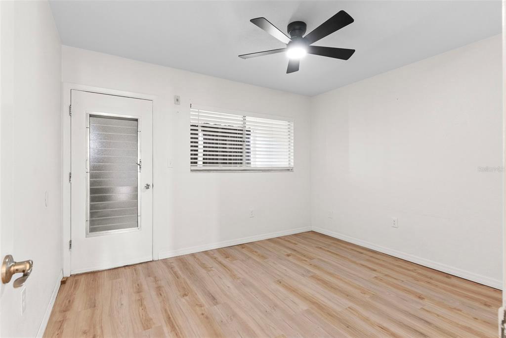 An empty room features light wood-look flooring, white walls, a ceiling fan, and a door — 11251 80TH AVENUE UNIT 307, SEMINOLE, FL