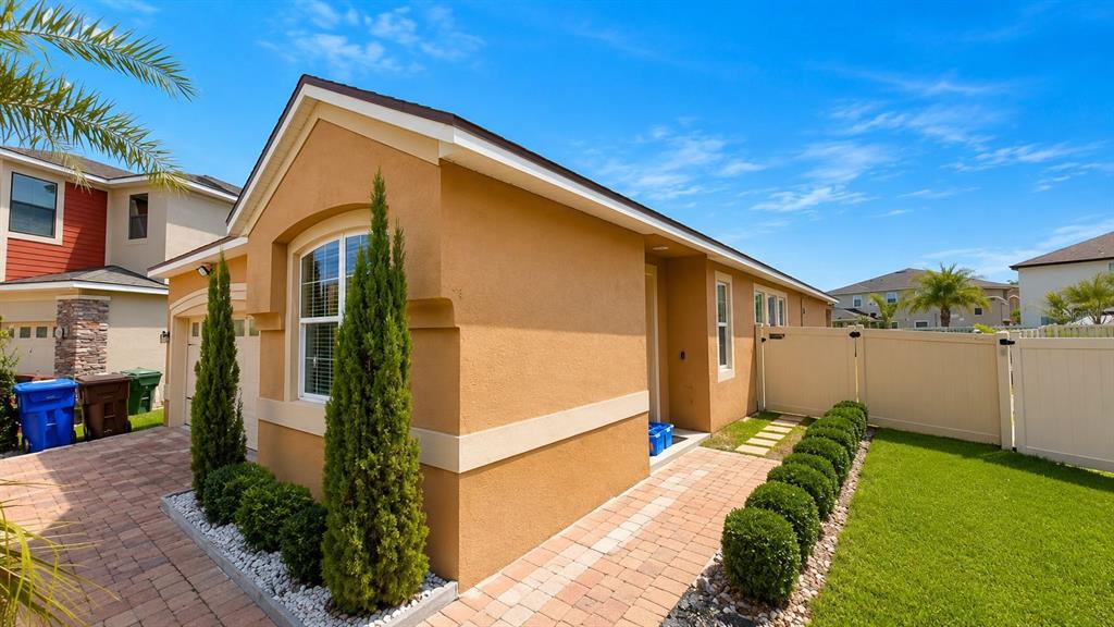 A tan single-story house with a paved driveway, a palm tree, and a two-car garage — 2608 NOUVEAU WAY, KISSIMMEE, FL