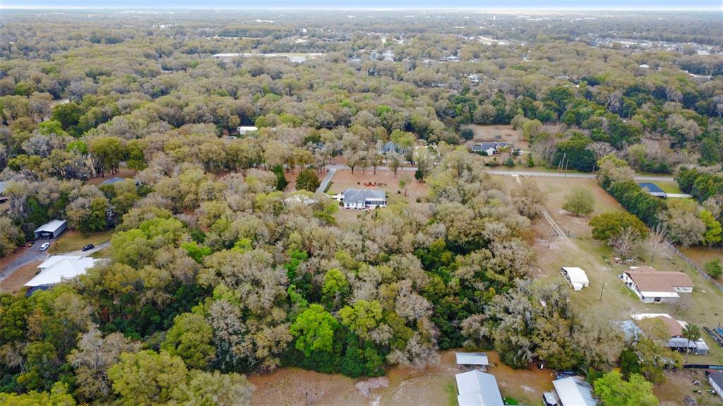 An aerial view shows a house nestled among dense trees in a rural residential area — N RIDGEWOOD AVENUE, DELAND, FL