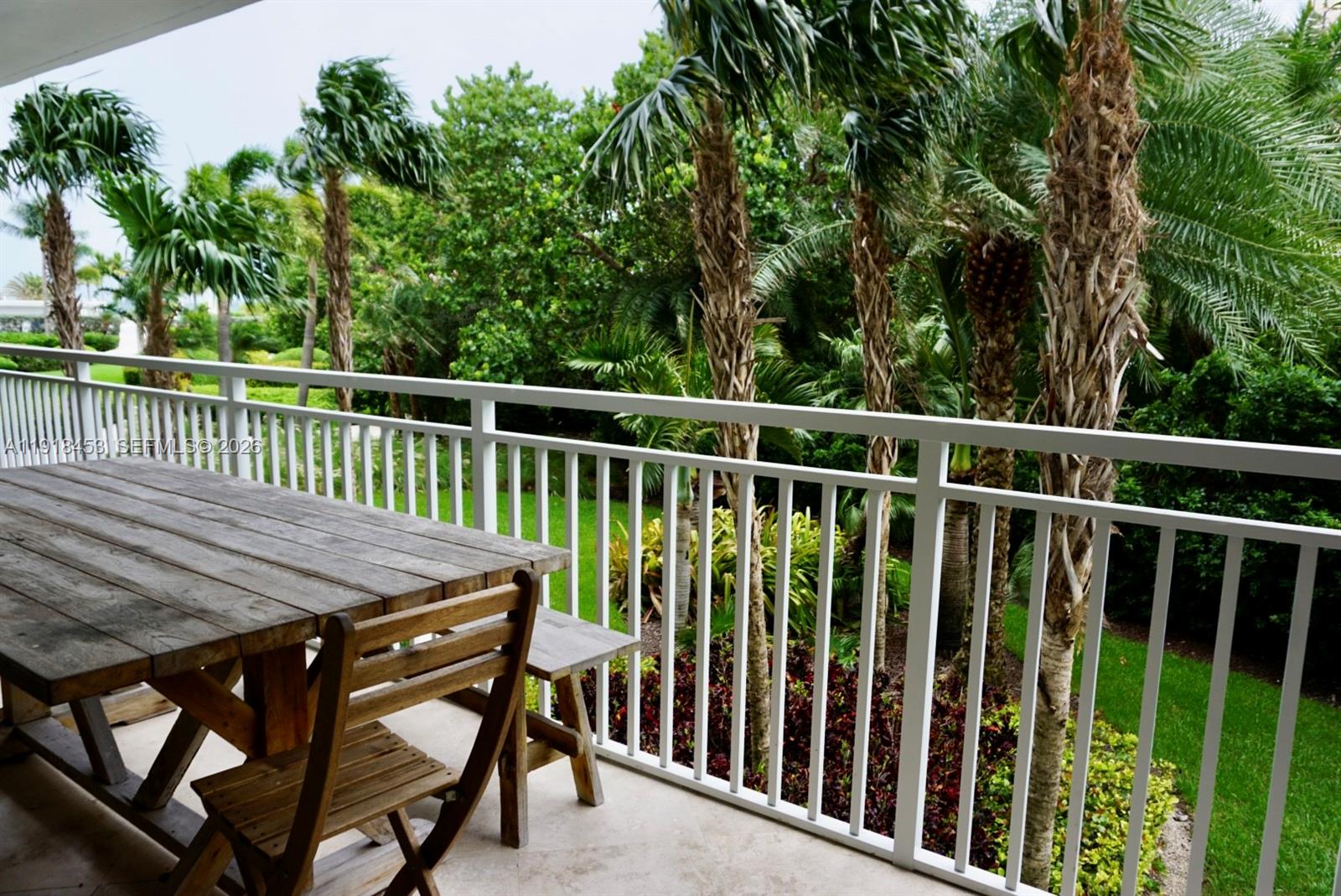 A wooden table and chairs sit on a balcony overlooking a lush, palm-filled garden — 605 Ocean Dr # 2L, Key Biscayne FL 33149, KEY BISCAYNE, FL