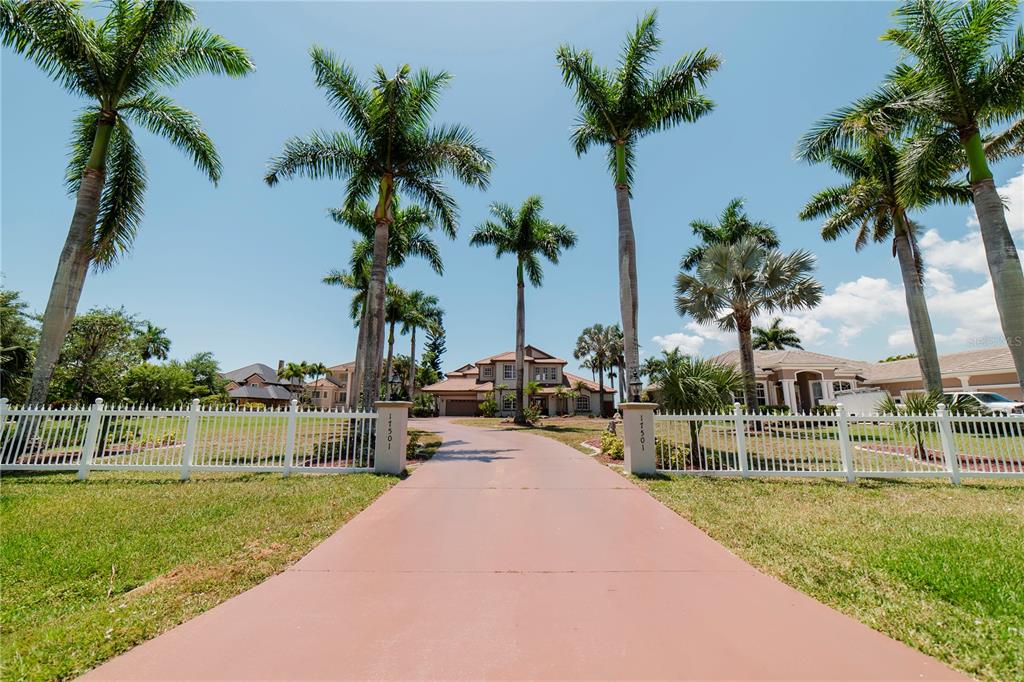 A long driveway leads to a two-story house framed by palm trees and white fencing — 17501 OHARA DRIVE, PORT CHARLOTTE, FL