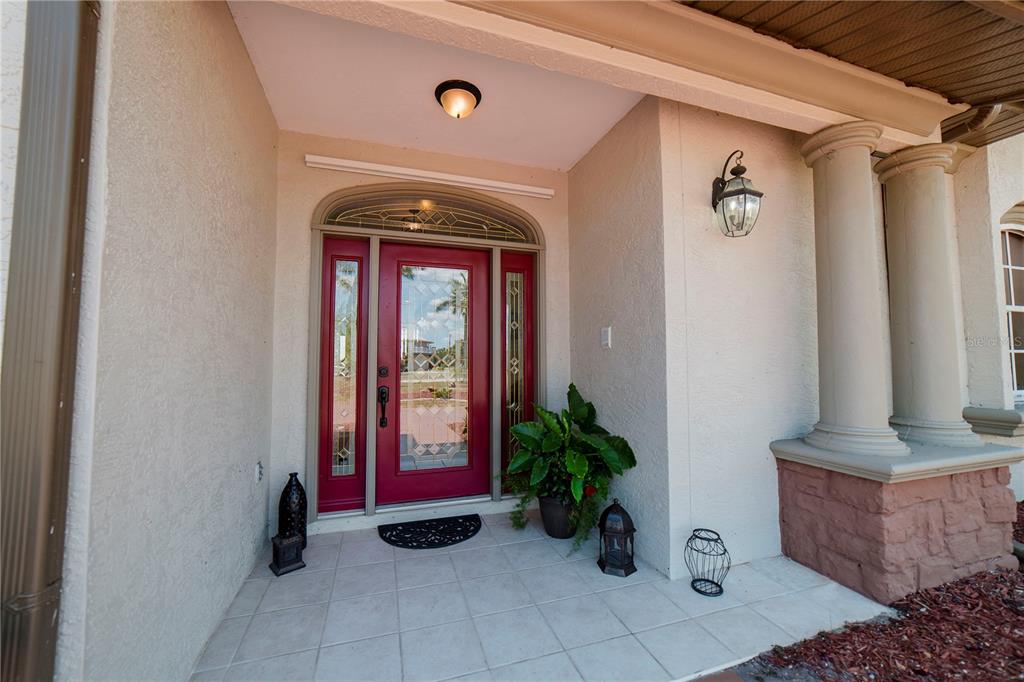A red front door with a glass insert sits under a covered entryway with columns — 17501 OHARA DRIVE, PORT CHARLOTTE, FL