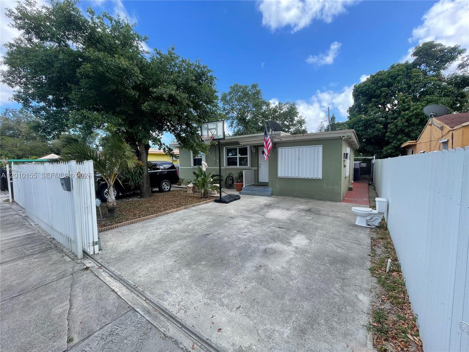 A single-story green house features a concrete driveway, a basketball hoop, and an outdoor toilet — 2144 NW 85th St, Miami FL 33147, MIAMI, FL