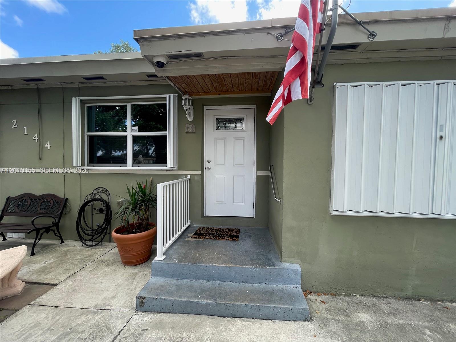 The exterior of a house features a white front door, steps, and an American flag — 2144 NW 85th St, Miami FL 33147, MIAMI, FL