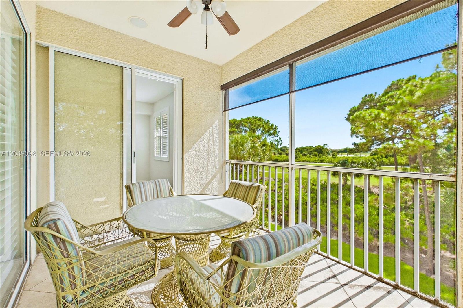 A screened-in balcony features a glass-topped table, four chairs, and a view of trees — BONITA SPRINGS, FL